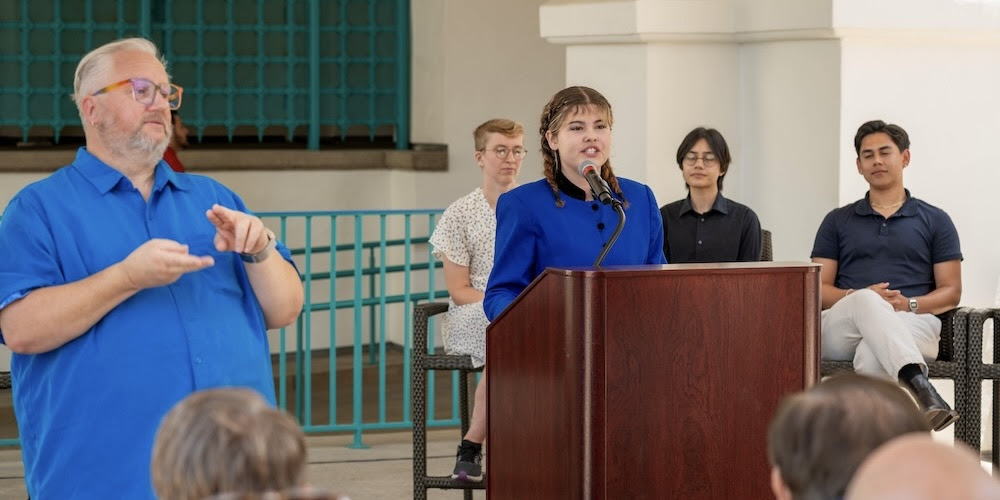 SDSU student giving a speech with an interpreter signing in sign language.